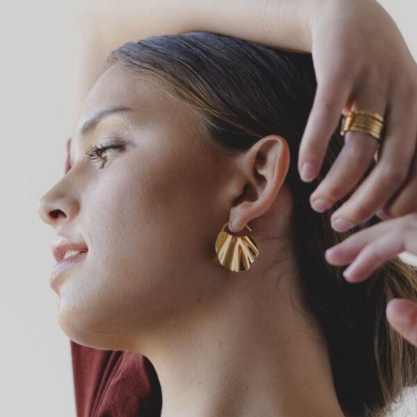 A person wearing a wavy gold earring, her arm over her head.