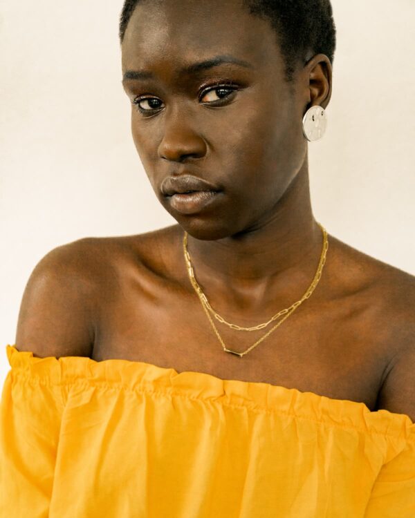 A portrait of a person wearing a yellow top and two gold necklaces.