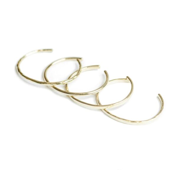 Four thin gold bangles set out on a white background.