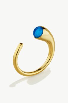 A U-shaped gold ring standing on edge on a white background. It has a blue piece of glass on a thick, horn shaped end.