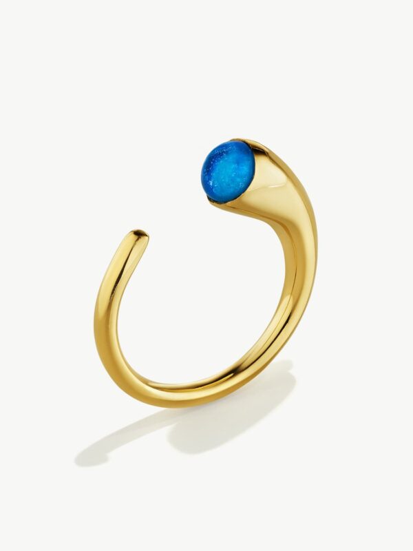 A U-shaped gold ring standing on edge on a white background. It has a blue piece of glass on a thick, horn shaped end.