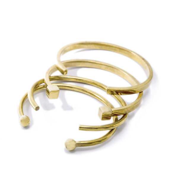 Four cuff-style gold bracelets on a white background with various shaped ends.