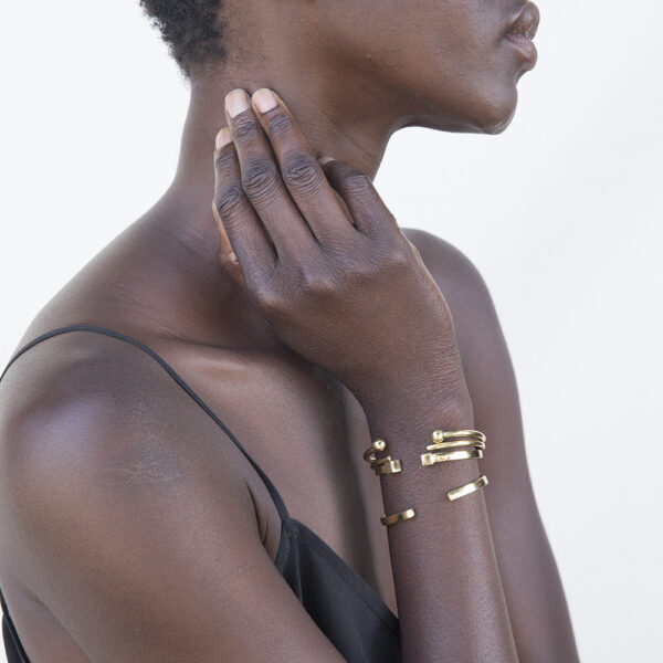 A person's arm, lifted to their neck, wearing four various shaped gold cuff bracelets.