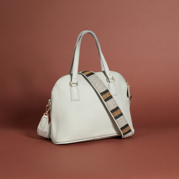 A light grey leather handbag with a zippered top, handles and a beaded brown, black, and white shoulder strap.