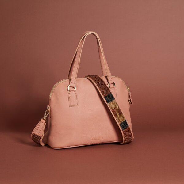 A muted pink leather handbag with a zippered top, handles and a beaded brown, black, and burgundy shoulder strap.