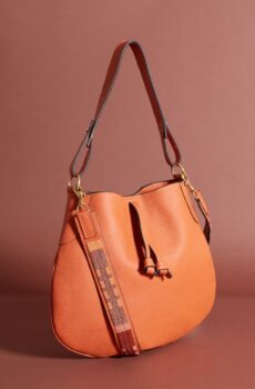 An orange saddlebag-style purse with a short strap, a drawstring, and a red and orange beaded shoulder strap