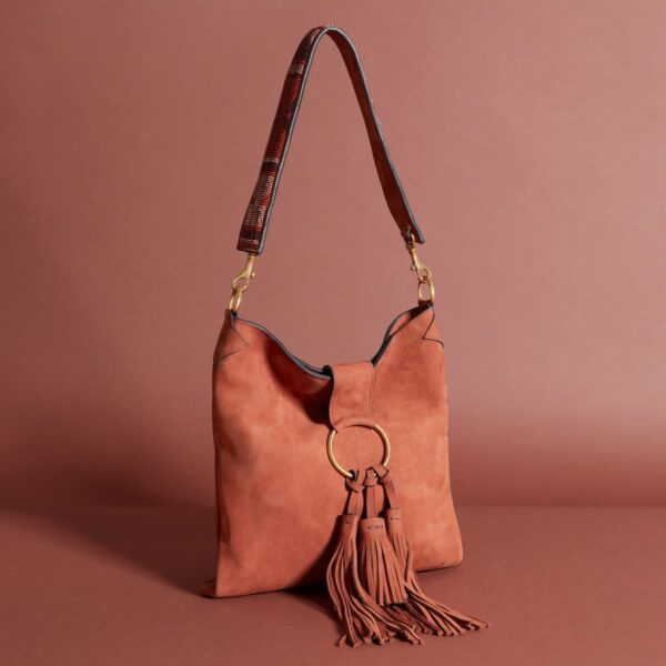 A warm cognag colored shoulder bag with a long shoulder strap and a large tassel attached to a metal ring on the closure