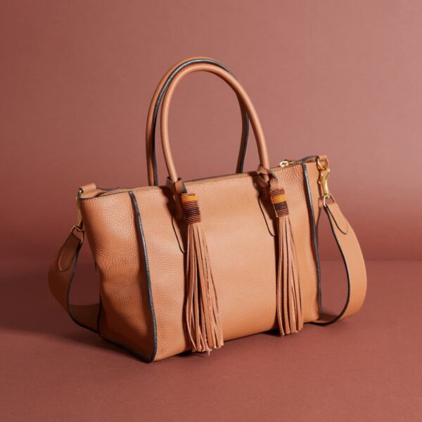 a warm tan leather bag with handles, a strap, and two tassels