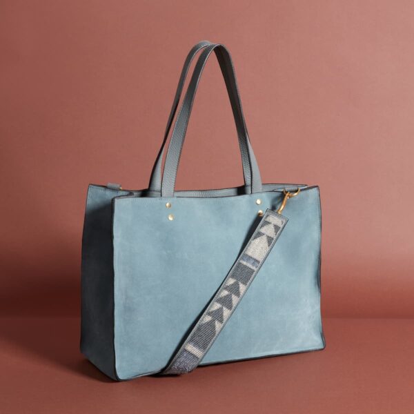 A blue-grey tote-style bag with long handles and a long grey and white beaded armstrap