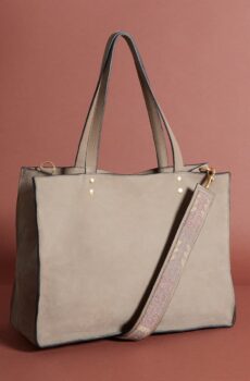 A taup leather tote-style bag with long handles and a simple beaded shoulder strap