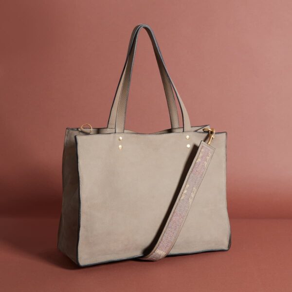 A taup leather tote-style bag with long handles and a simple beaded shoulder strap