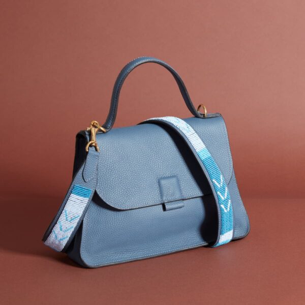 A blue leather bag with a handle, a blue and white beaded shoulder strap, and a fold-over magnetic flap