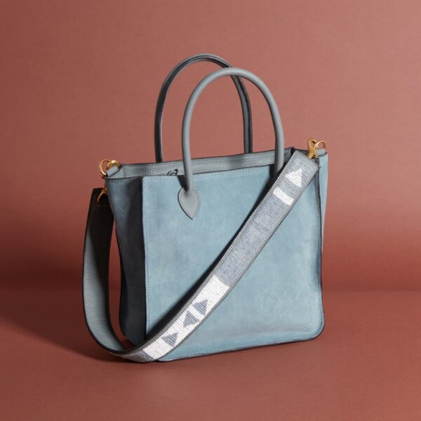 A blue-grey leather tote-style bag with handles and a long grey and white beaded shoulder strap