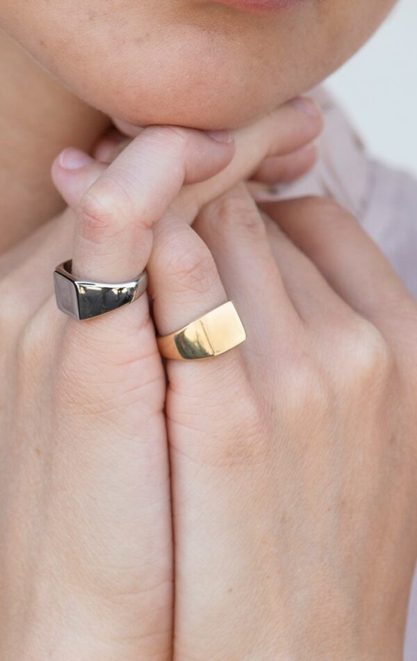 person wearing two signet pinky rings. One made of recycled brass plated in chrome the other made of 24k gold-plated recycled brass
